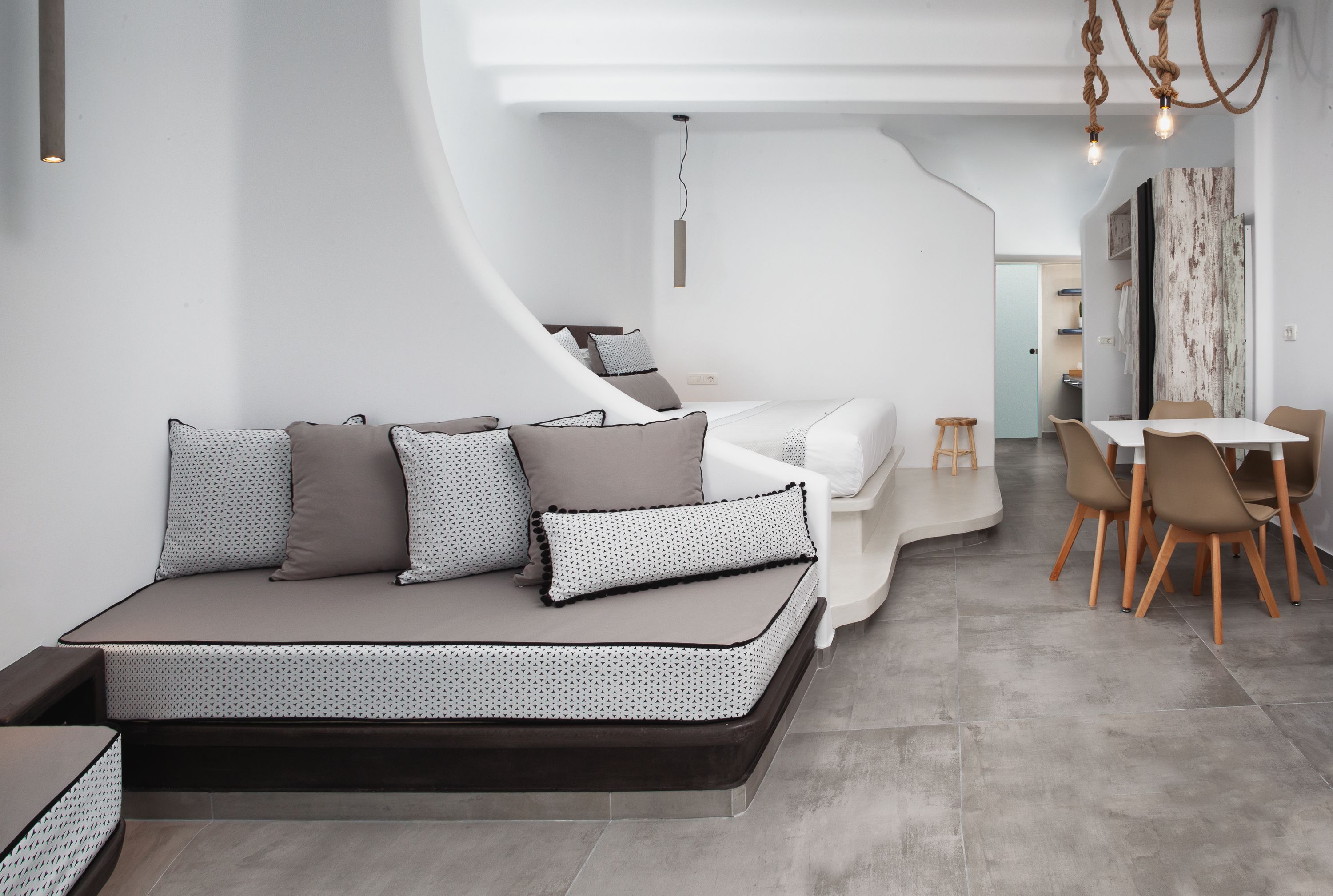 A modern, compact living space with a sofa bed, a dining area with chairs, and a kitchen in the background.