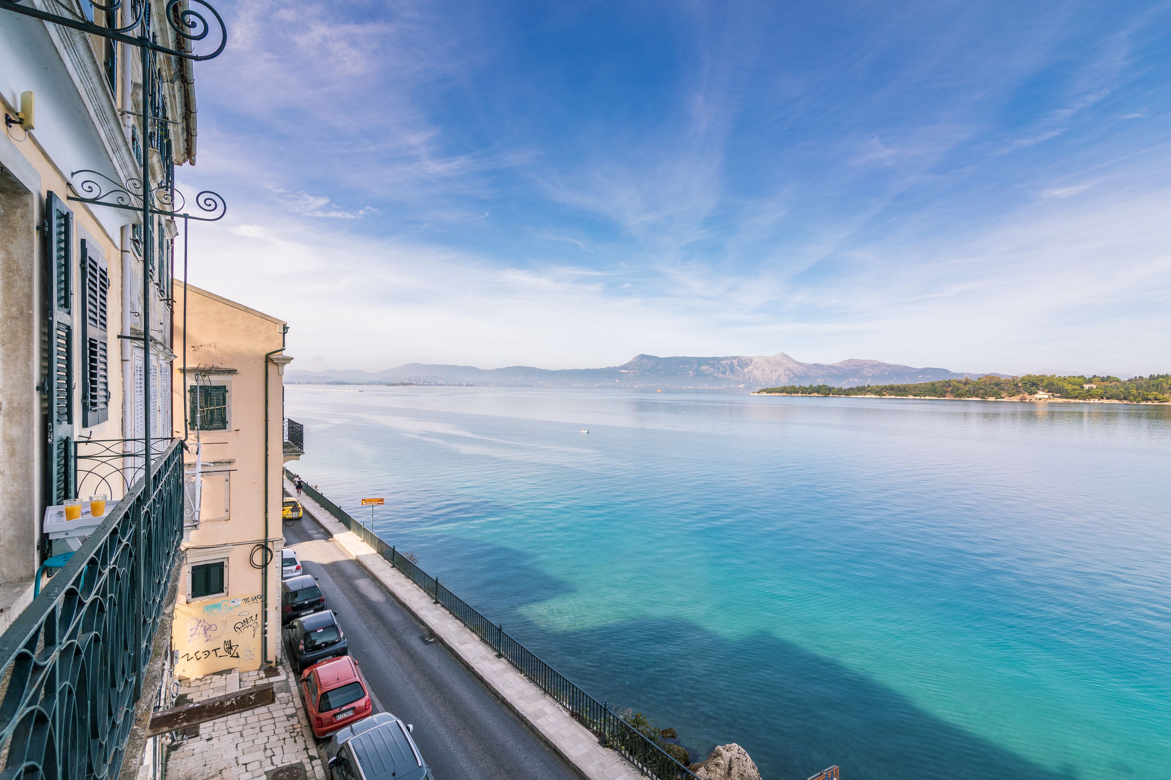 A coastal street with parked cars, a clear sky, and a calm sea.