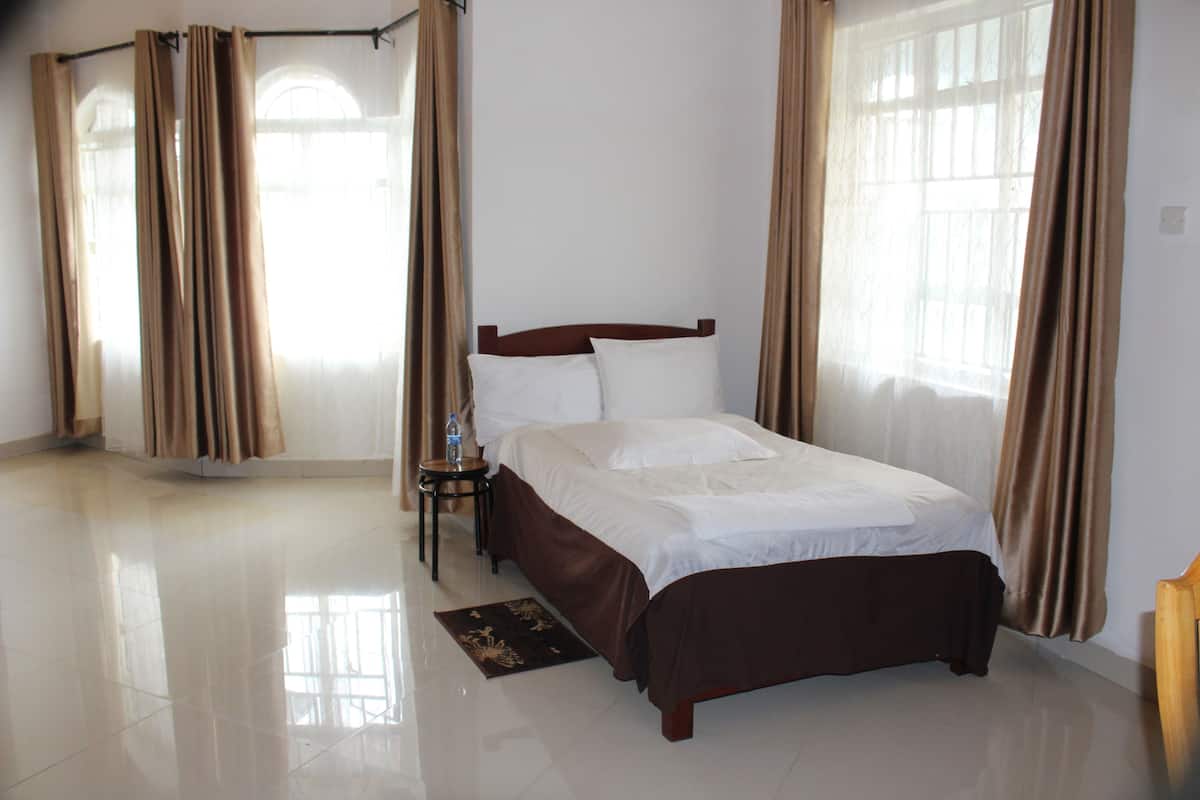 Quarto de hotel com uma cama grande, uma mesinha de cabeceira e uma janela com cortinas.