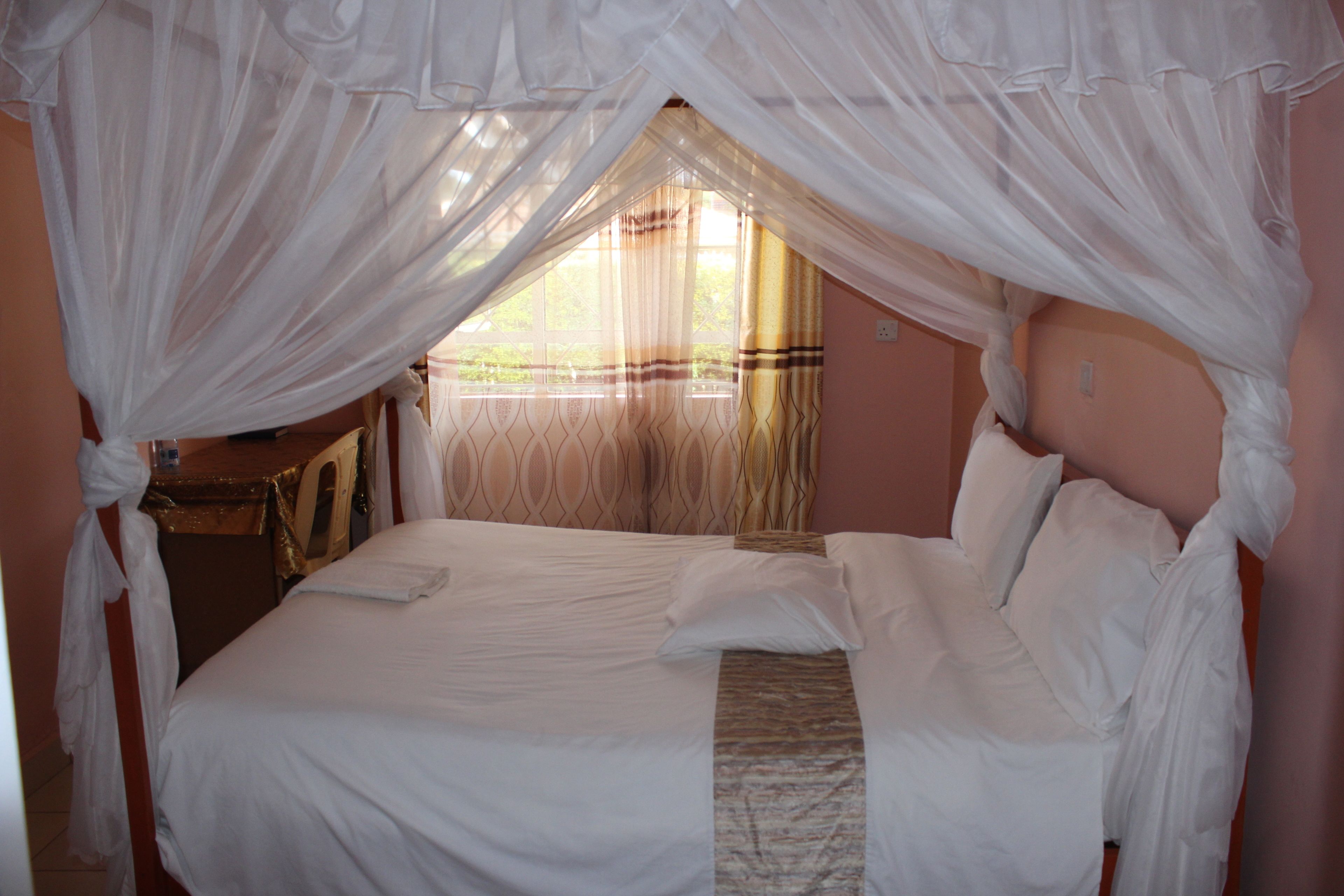 A bed with white bedding, a canopy, and a view of greenery outside.