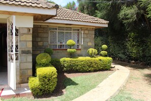 A stone house with a tiled roof, a window with a white frame, and well-maintained hedges. - Salient Guest House (Eldoret)