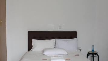 Una cama bien hecha con sábanas blancas, un cabecero marrón y una mesita de noche con una botella de agua.
