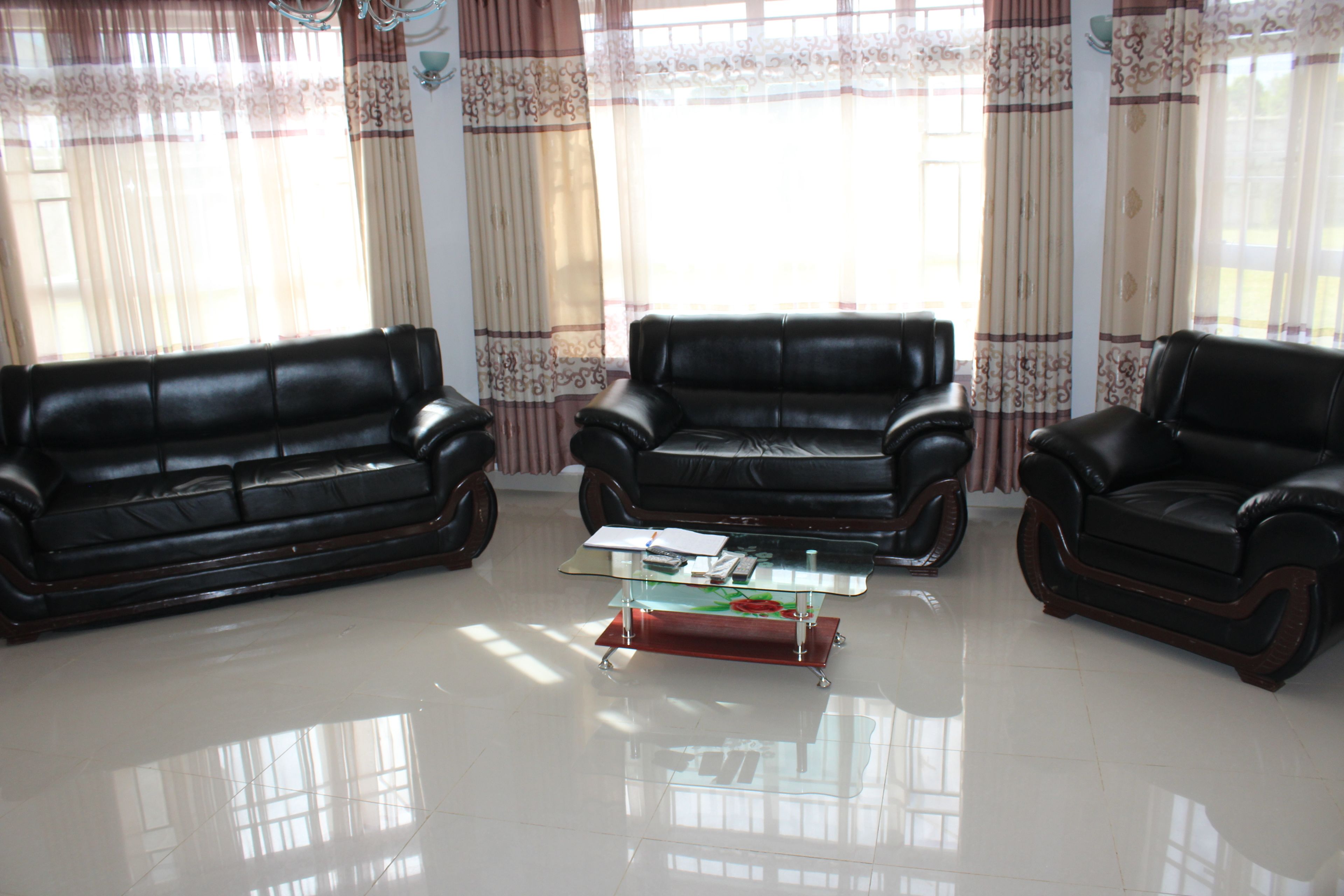 A living room with three leather sofas, a glass coffee table, and curtains.