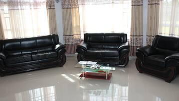 A living room with three leather sofas, a glass coffee table, and curtains.