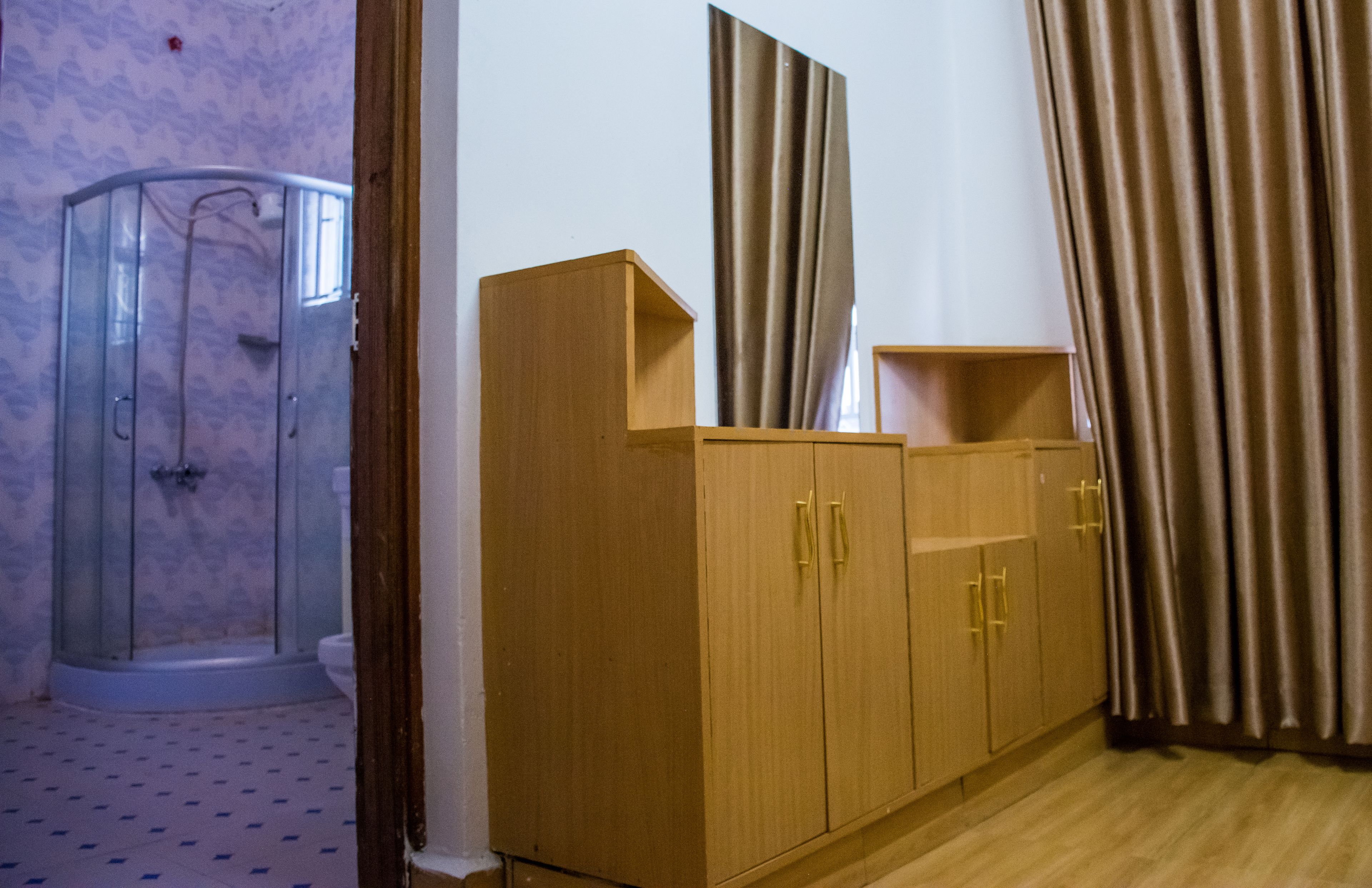 A room with a shower enclosure, wooden cabinets with gold handles, and a curtain.