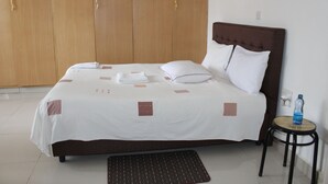 A neatly made bed with white linens and a brown headboard, a wooden wardrobe, and a small round table with a water bottle. - Salient Home Stay (Eldoret)