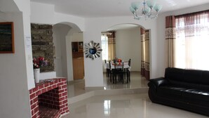 A living room with a black leather sofa, a fireplace, a dining area with a table and chairs, and a kitchen in the background. - Salient Home Stay (Eldoret)