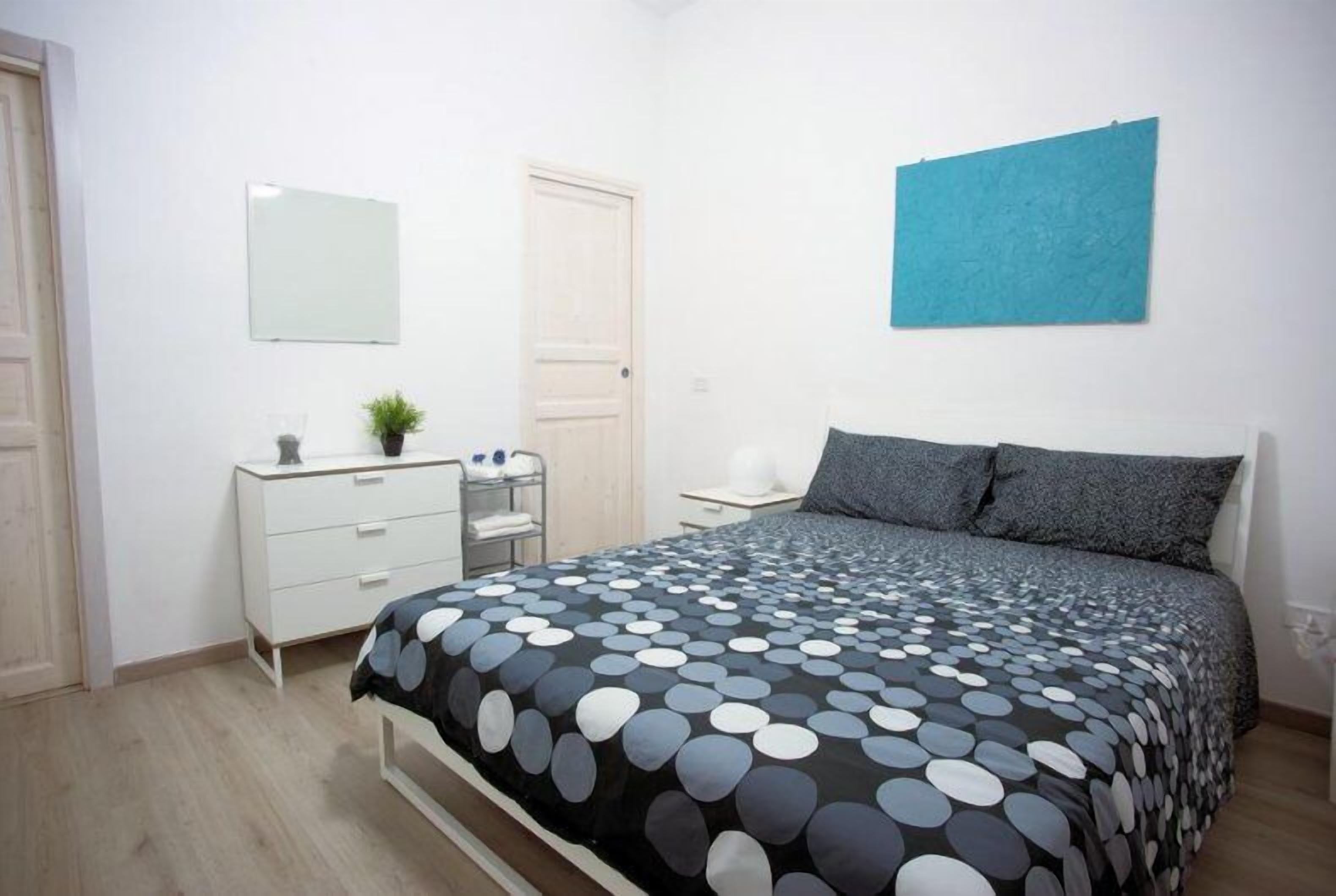 A bedroom with a bed, a dresser, a mirror, a blue wall hanging, and a door.