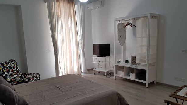A bedroom with a bed, a TV on a stand, a wardrobe, and a chair.