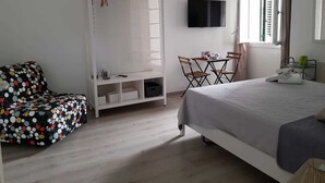 A bedroom with a bed, a white wardrobe, a small table with chairs, and a TV on the wall.