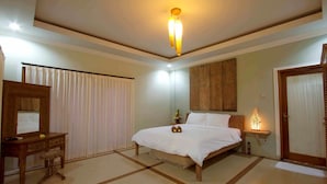 A hotel room with a bed, a wooden dresser, a mirror, a bedside table with a lamp, and a door. - Villa Go (Kerobokan Kaja)