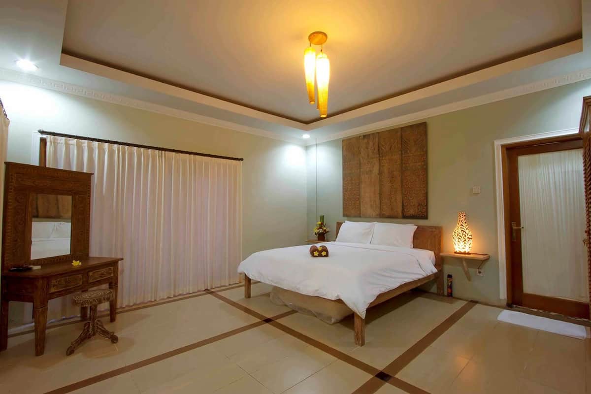A hotel room with a bed, a wooden dresser, a mirror, a bedside table with a lamp, and a door.