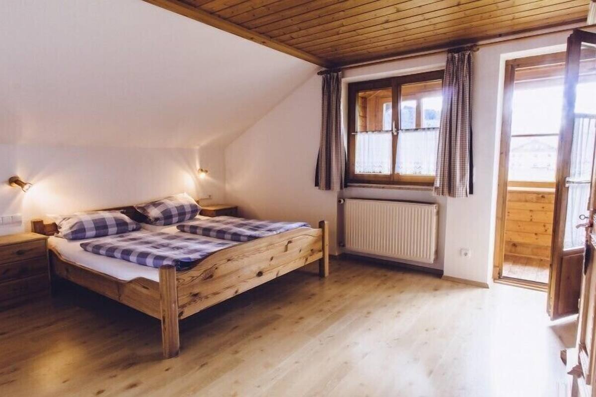 Ein Schlafzimmer mit einem hölzernen Bett, einem Nachttisch, einem Fenster mit Vorhängen und einer Heizung.