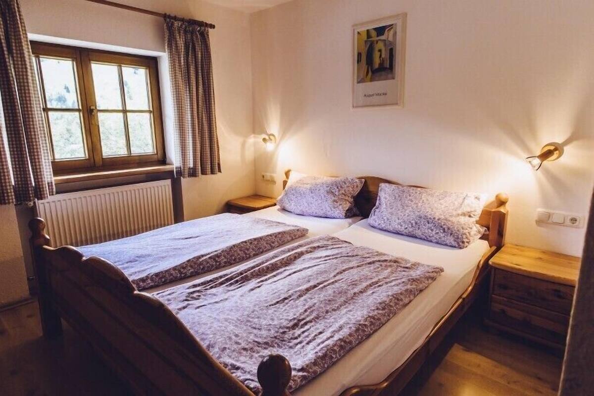 Ein Doppelbett mit Holz Kopfteil, zwei Nachttische mit Lampen, ein Fenster mit Vorhängen und ein gerahmtes Bild an der Wand.