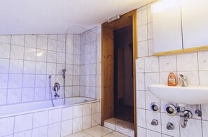 Un baño con bañera, puerta de madera y lavabo con dispensador de jabón.