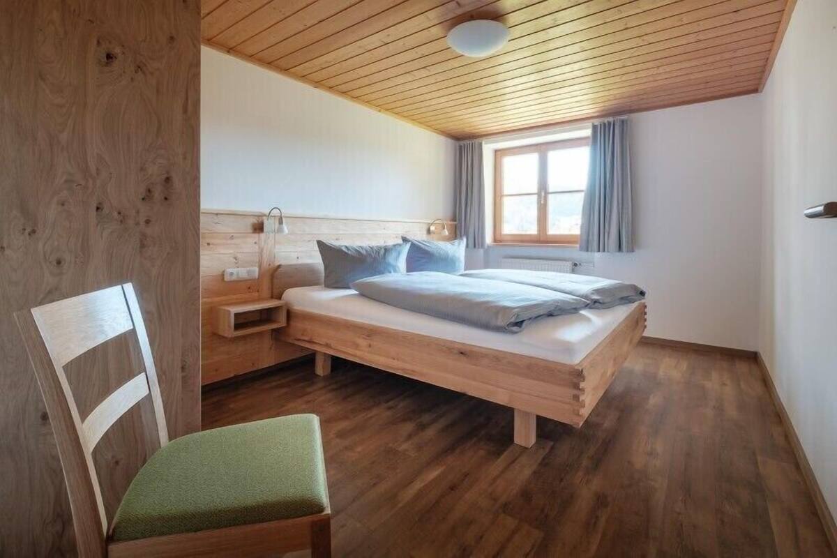 Ein Schlafzimmer mit einem hölzernen Bett, einem Nachttisch, einem Stuhl und einem Fenster mit Vorhängen.