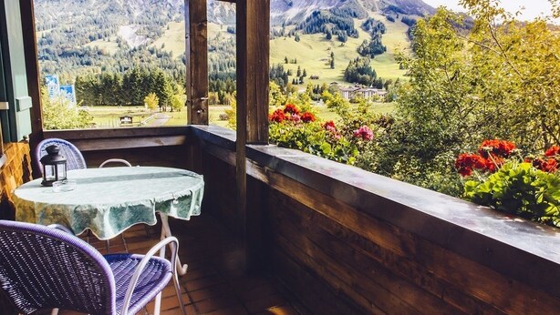A wooden balcony with a table and chairs, overlooking a mountainous landscape with greenery and flowers. - Haflingerhof - Kematsried (Bad Hindelang)