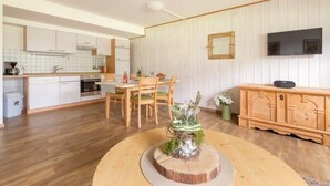 A modern kitchen with white cabinets, a dining area with wooden chairs, and a TV mounted on the wall. - Haflingerhof - Kematsried (Bad Hindelang)