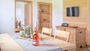 A dining area with a wooden table, chairs, a bottle of wine, a small plant, and a bookshelf. - Haflingerhof - Kematsried (Bad Hindelang)