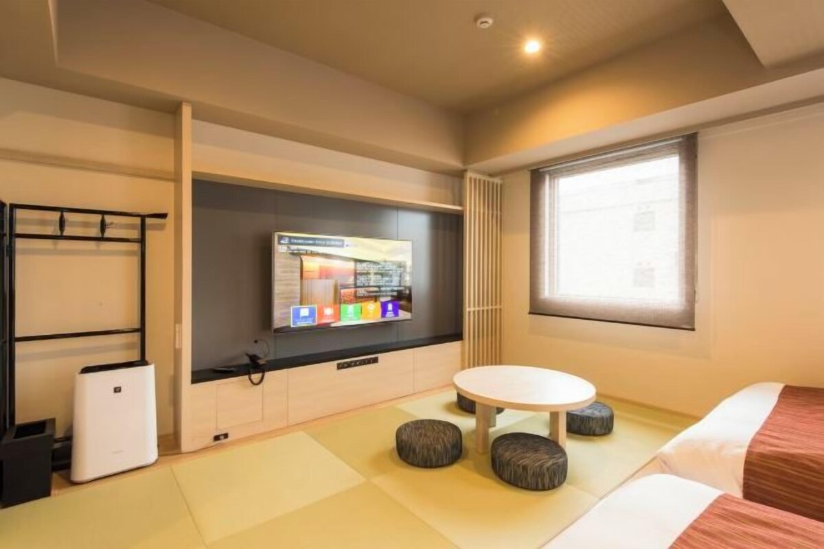 A hotel room with a bed, a small table, a TV, and a window.