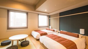Une chambre d’hôtel moderne avec deux lits, une petite table ronde et un coin salon avec des poufs.