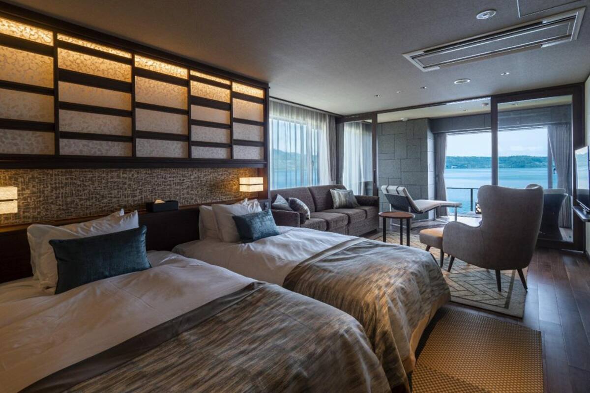 A hotel room with two beds, a sofa, a chair, and a view of the sea.