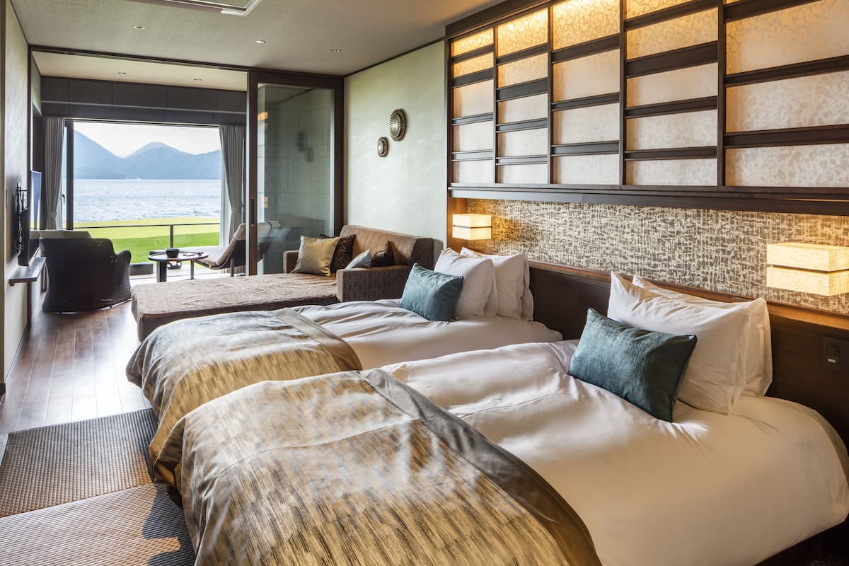 A hotel room with a large bed, a sofa, a small table, and a view of the sea.