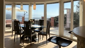 Ein Essbereich mit Tisch und Stühlen, große Fenster mit Meerblick und ein Balkon mit Gartenmöbeln.