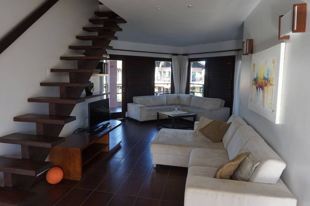 A modern living room with a staircase, a white sofa, a coffee table, and a TV.