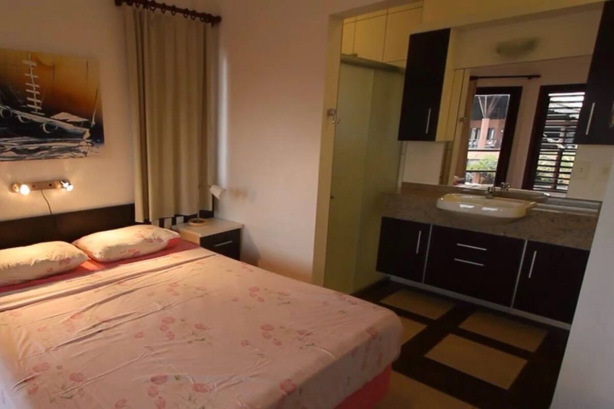A bedroom with a bed, nightstand, and a bathroom with a sink and mirror.