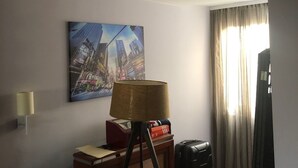 A hotel room with a cityscape painting, a lamp, a suitcase, and a desk with a lamp. - Beo-River Chocolate (Belgrade)