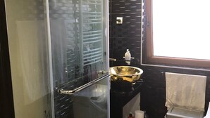 A modern bathroom with a glass shower enclosure, a black tiled wall, a sink with a gold basin, and a red rug. - Beo-River Chocolate (Belgrade)