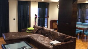 A modern living room with a large L-shaped brown leather sofa, a glass coffee table, and a wooden floor. - Beo-River Chocolate (Belgrade)