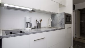 A modern kitchen with white cabinetry, a built-in coffee maker, and a marble countertop.