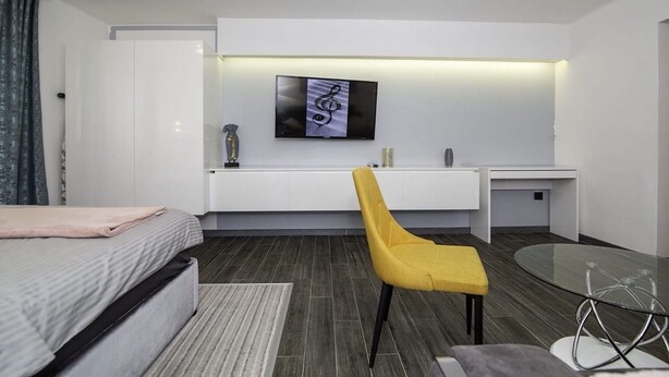 A modern hotel room with a bed, a desk with a chair, a flat-screen TV, and a glass table.