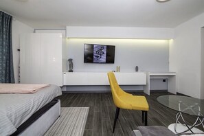 A modern hotel room with a bed, a desk with a chair, a flat-screen TV, and a glass table. - Beo-River White (Belgrade)
