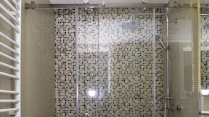 A modern bathroom with a glass-enclosed shower, a white sink, and a tiled mosaic wall.