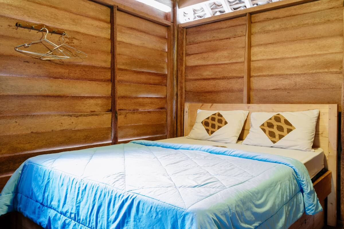 Ein Zimmer mit Holzwänden, einem Bett, zwei Kissen mit Rautenmuster und einem Kleiderständer.