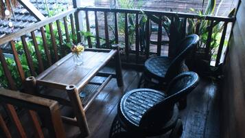 Um deck de madeira com uma mesa e duas cadeiras, cercado por plantas e um cercado de bambu.