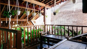 Um deck de madeira com vasos suspensos, uma mesa e uma estrutura de telhado de palha.