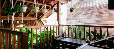 A wooden deck with hanging planters, a table, and a thatched roof structure.