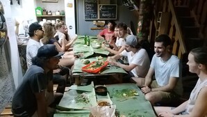 Un groupe de personnes est assis autour d’une longue table recouverte d’une nappe verte et prend son repas.