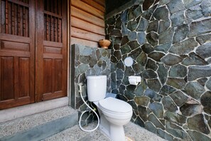 A bathroom with a stone wall, a wooden door, and a toilet. - Good Karma Yogyakarta - Hostel (Yogyakarta)
