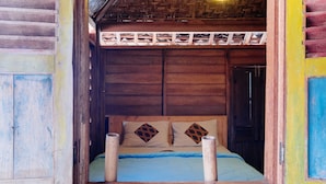 Une pièce en bois avec un lit, une porte en bois et un plafond fait de fibres tressées.