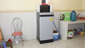 A compact kitchen with a refrigerator, microwave, and a sink. There is a broom and a chair in the corner. - Chambre en Ville (Sen Monorom)