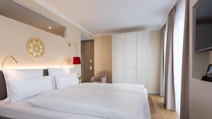 A hotel room with a large bed, a chair, a wardrobe, and a television.