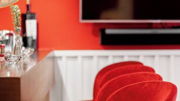 Una zona de bar con una pared roja, un televisor de pantalla plana y tres taburetes de terciopelo rojo.