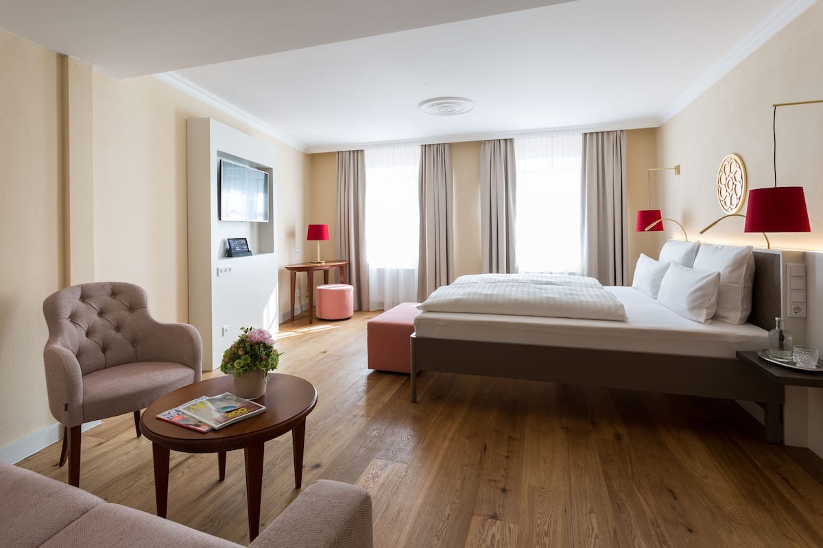 Habitación de hotel con cama, una silla, una mesita, televisor y ventana con cortinas.