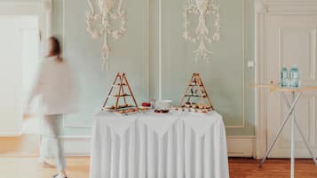 A room with a white table covered with a white tablecloth, two wooden display stands with food items, and a small table with bottles.