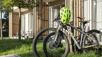 Una bicicleta de montaña con casco verde estacionada sobre césped frente a un edificio con ventanas amplias y una valla de madera.